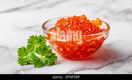 A bowl of red caviar decorated with a sprig of parsley on a marble countertop. The warm light and detailed texture create a fresh and appetizing mood, Stock Photo