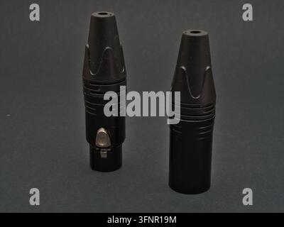 Two Black XLR Connectors on Dark Backgro - Two professional black XLR audio connectors are shown on a dark gray surface, ideal for sound equipment and Stock Photo