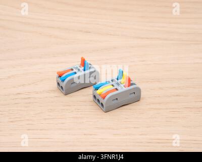 Electrical Wire Connectors on Wood - Two modern electrical wire connectors, featuring blue, orange, and yellow levers, are arranged on a light-colored Stock Photo