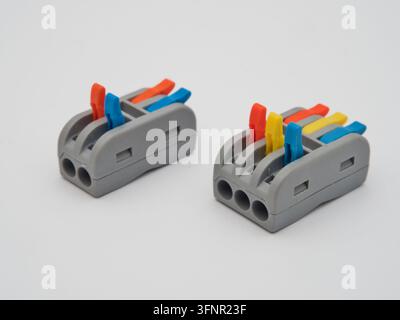 Colorful Electrical Wire Connectors - Two gray electrical wire connectors with vibrant orange, blue, and yellow levers are arranged on a clean white b Stock Photo