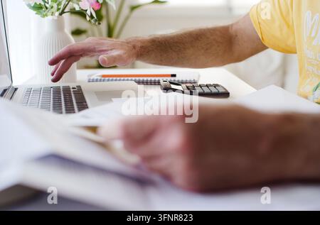 Hands organizing documents, entering numbers on a laptop and using a calculator for home office tax preparation, budgeting and financial planning at a Stock Photo