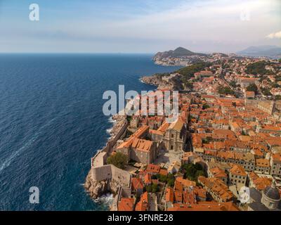 Dubrovnik Croatia stretches along Adriatic coast, its old stone city enclosed by fortified walls. Orange roof tiles, rocky cliffs and blue sea define Stock Photo