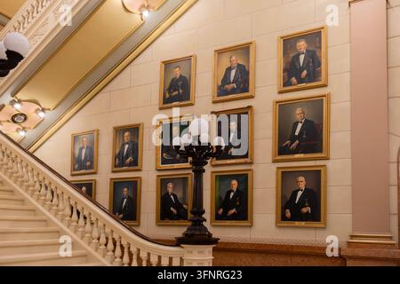 Philadelphia, Pennsylvania - August 29, 2026: Elegant view of gilded framed portraits along staircase wall behind decorative multi-globe lantern. Stock Photo