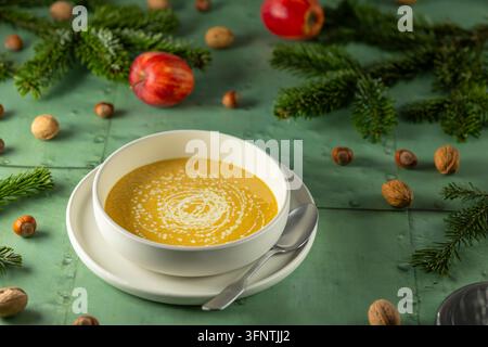 Creamy soup in a white bowl garnished with a swirl of cream, surrounded by festive elements Stock Photo