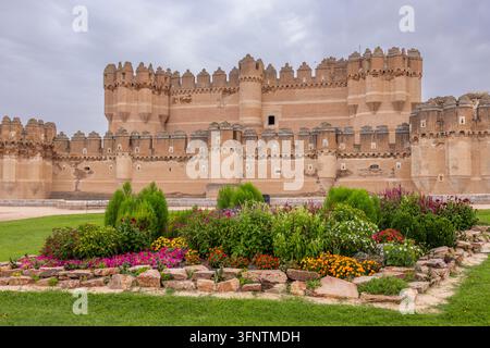 Ancient brick castle standing behind a vibrant flower garden on a cloudy day Stock Photo