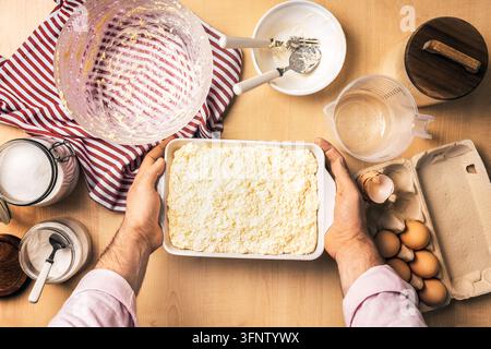 Man holding baking dish with raw cottage cheese casserole before oven. Preparing sweet curd cake, fresh homemade recipe with eggs, sugar, flour, and t Stock Photo