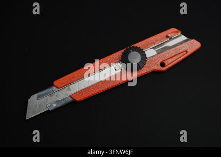 An orange textured heavy-duty utility cutter knife with a black safety locking screw knob, placed diagonally on a solid black background. Stock Photo