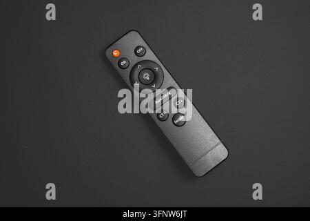 Top view of a black smart LED lighting remote control with buttons, placed diagonally on a dark gray textured background. Stock Photo