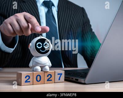 Business professional interacting with AI robot beside 2027 blocks while using laptop. Enterprise AI adoption, automation strategy, digital transforma Stock Photo