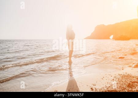 Woman beach sunset young female in black swimsuit stands on sandy shore while bright sunlight glows over rocky cliffs Stock Photo