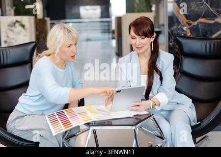 Two professional women engage in a collaborative discussion within a contemporary office space, emphasizing teamwork and productivity. The image highl Stock Photo