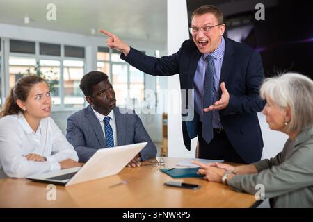 Angry middle-aged man shouting at his business partners sitting around table in conference room Stock Photo