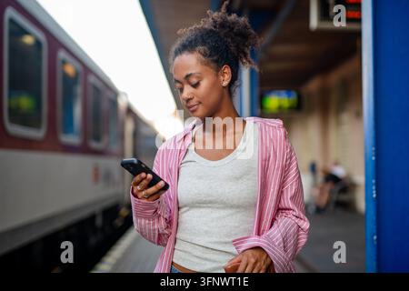 Female college student waiting for train, scrolling on phone. Stock Photo