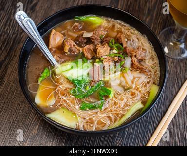 Deep clay bowl is filled with hot noodle soup and veal fillet. Shallots or green onions are added to dish for flavor. Stock Photo