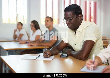 Concentrated african american man listening attentively and taking notes of lecture during adult education class Stock Photo