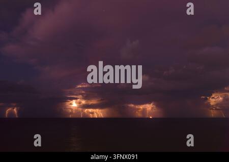 Dramati view of a severe thunderstorm over the ocean at night, featuring multiple lightning strikes illuminating dark storm clouds and Stock Photo