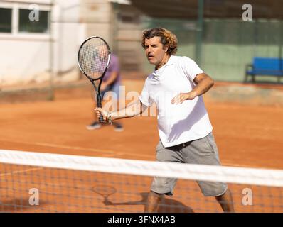 Handsome athletic man serving with racket in hands while practicing on tennis court in day Stock Photo