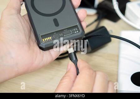 Close-up of hands connecting a USB cable to a portable magnetic power bank battery pack. Top view. Stock Photo