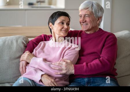 Peaceful happy senior couple embracing on couch and enjoying each other company and conversation. Stock Photo