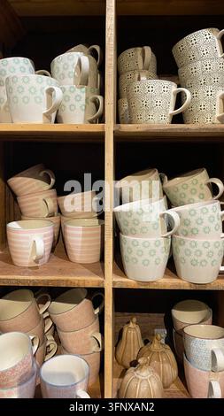 Colorful patterned ceramic coffee mugs arranged on wooden shelves in home decor shop Stock Photo