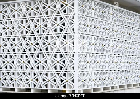 Modern white ventilation roster blocks featuring intricate Islamic geometric patterns with gold star accents on a building wall Stock Photo