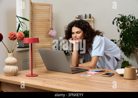 Curly-haired woman focused on her laptop at home, embracing mindful work and comfort Stock Photo