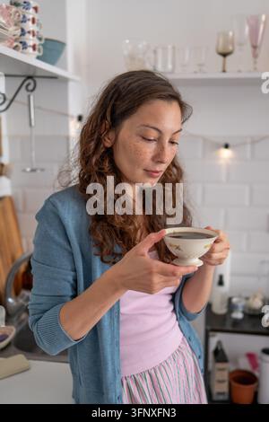 Calm young woman enjoying hot black coffee at home, taking relaxing mindful morning break in kitchen Stock Photo