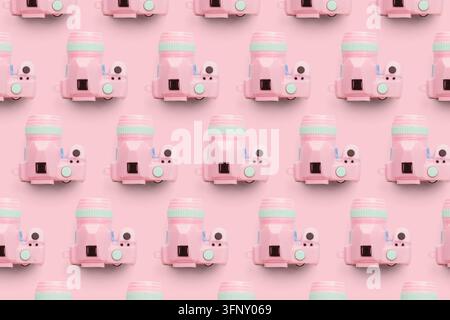 Flat lay pattern featuring small pink toy cameras with mint accents arranged in a grid on a monochromatic pink surface. Stock Photo
