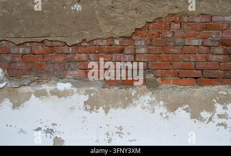 Deteriorating white painted concrete and red brick masonry wall with exposed brickwork, crumbling concrete, horizontal cement gap, worn mortar Stock Photo