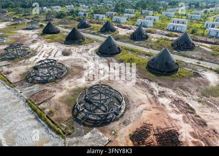 Aerial view of an abandoned building project featuring cone-shaped structures and circular concrete frames amidst unfinished white houses in Karangan, Stock Photo