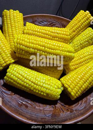 Fresh yellow corn on the cob arranged in a rustic bowl, close-up view of ripe sweet corn ready for cooking. Stock Photo