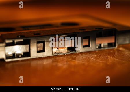 Detailed macro photograph highlighting the exposed magnetic tape and inner mechanism of a black audio cassette sitting flat on a warm wooden surface. Stock Photo