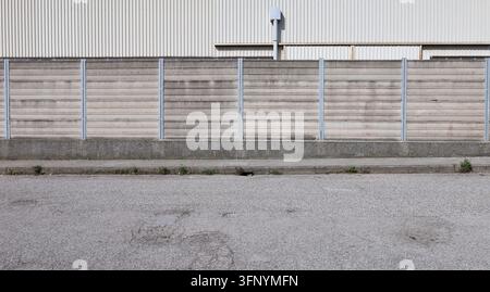 Concrete precast compound wall, reinforced with metal slats. Road in front, white industrial building on behind. Background for copy space Stock Photo