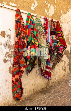 Handmade colorful Berber carpets hanging on a textured wall in the medina of Essaouira, Morocco. Stock Photo