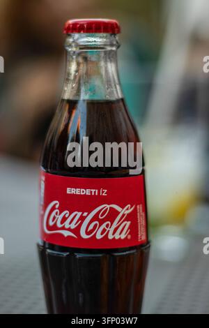 hungary, budapest 2021 04 30: Close-up vertical view of a classic glass Coca-Cola bottle with red cap and label, soft natural daylight, shallow depth Stock Photo