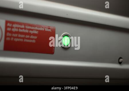 hungary, budapest 2021 09 05: Close-up shot of a glowing green door opening button on a public train interior, horizontal perspective with natural int Stock Photo