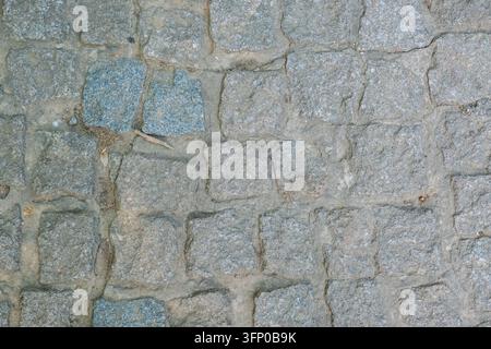 Weathered gray and blue stone cobblestone pavement with rough rectangular blocks, mortar joints, cracks, dirt, and small natural debri Stock Photo