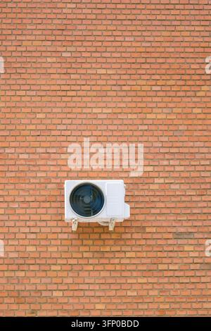 White outdoor air conditioner mounted on a red brick wall with a centered circular fan, visible brackets, and generous blank architectural copy spac Stock Photo