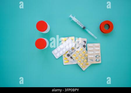 Syringe, red-capped specimen containers, assorted tablets and capsules in blister packaging arranged on a turquoise surface with open compartment Stock Photo
