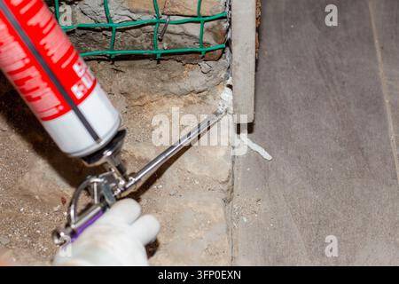 A close up of a construction worker using a metal foam gun to fill gaps with polyurethane foam. Professional residential renovation process. Home impr Stock Photo
