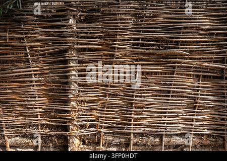 Wattle fence background. Traditional rustic braided wooden fence made of twigs and branches. Stock Photo