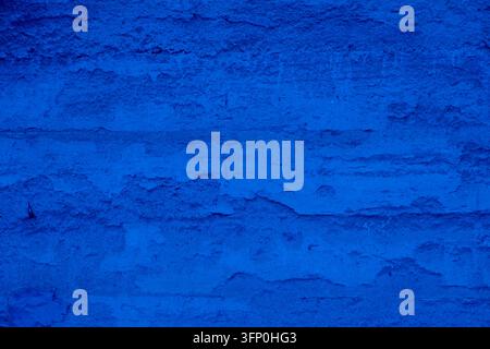 Weathered grunge cement surface painted in solid classic blue color with heavily distressed uneven texture and cracks, perfect for abstract dark backg Stock Photo
