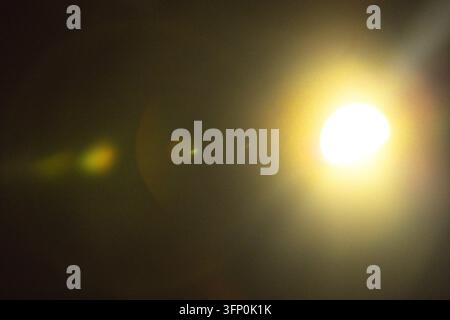 Bright circular light glows on the right against a dark background, creating a warm yellow halo and faint green lens flare in low light Stock Photo