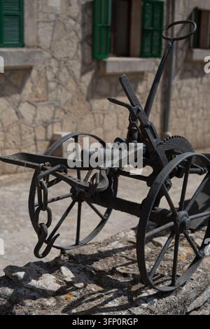 A close-up vertical shot of an old, weathered cast iron farm implement with large spoked wheels and a metal chain, resting on a textured stone wall. T Stock Photo