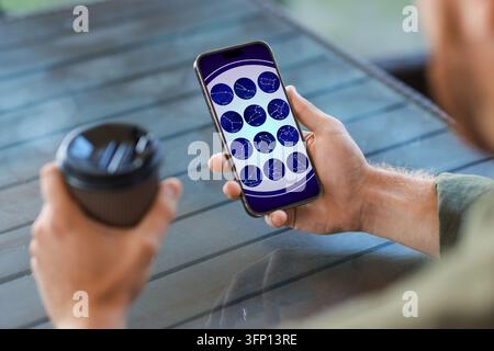 Man using astrology app on his smartphone while drinking coffee at table outdoors, closeup Stock Photo