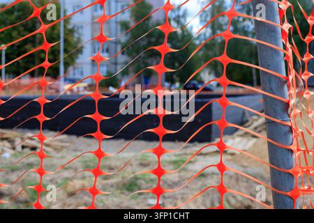 Orange plastic safety net barrier around construction site for danger caution concept. Temporary protective mesh fence installed near urban building a Stock Photo