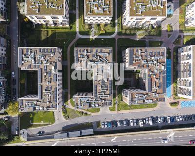 Aerial view of a modern residential development with U-shaped buildings, green roofs, solar panels, and HVAC systems, surrounded by walkways and parki Stock Photo