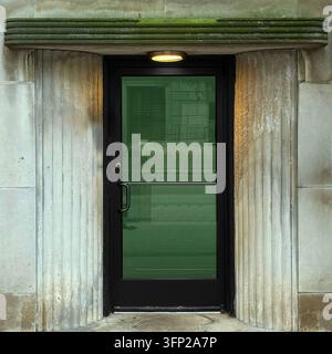 Green-tinted glass door under stone canopy and  rounded ribbed lintel and a glowing overhead light. Stock Photo