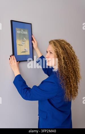 She diligently and accurately lines up framed art pieces on wall Stock Photo