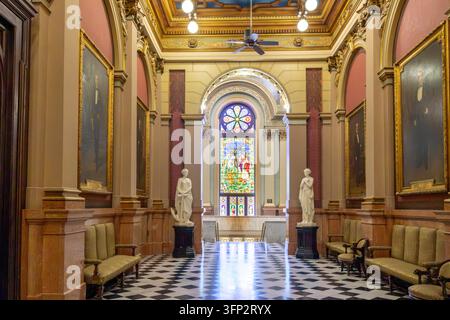 Philadelphia, Pennsylvania - August 29, 2026: Symmetrical view of classical marble statues, checkerboard floor, and colorful stained glass window in g Stock Photo